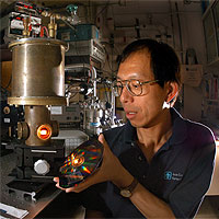 THE REAL HARRY POTTER? — A tungsten photonic lattice glows in a vacuum chamber as Sandia researcher Shawn Lin inspects an irridescent disk that contains approximately 1,000 tungsten photonic lattices. Most emissions from these filaments are in the near-infrared range, and may improve efficiencies of heat-driven engines like hybrid electric automobiles.
<P>(Photo by Randy Montoya) Courtesy Sandia National Labs.

